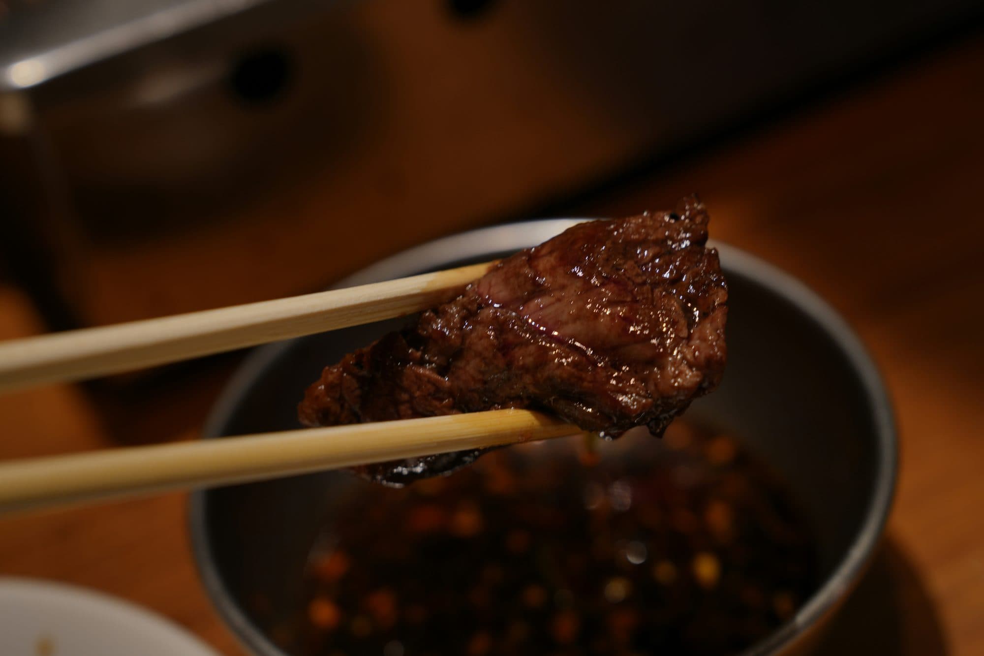 焼き上がった赤身をひと切れ、箸で持ち上げたところ。奥にタレの小鉢
